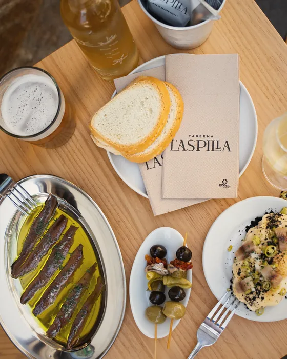 Mesa servida con anchoas, pan, aceitunas y la servilleta de L'Aspilla